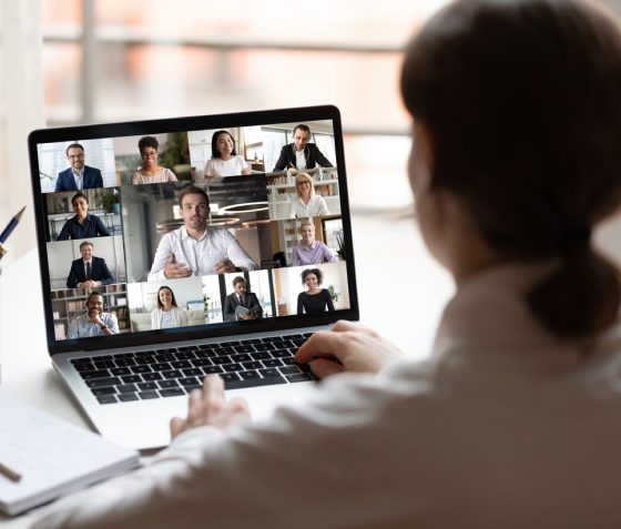 A person on a conference video call with thirteen people on a laptop